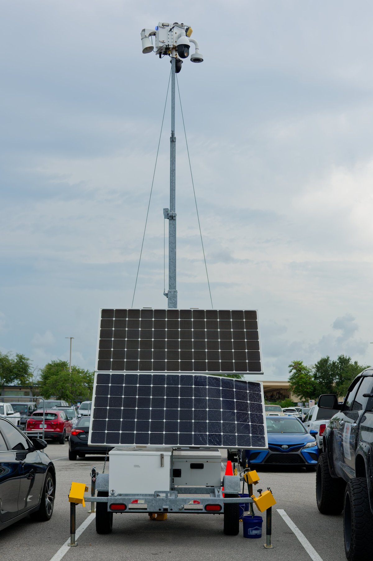 Mobile surveillance camera trailer with multiple cameras on a telescoping tower in a parking lot.