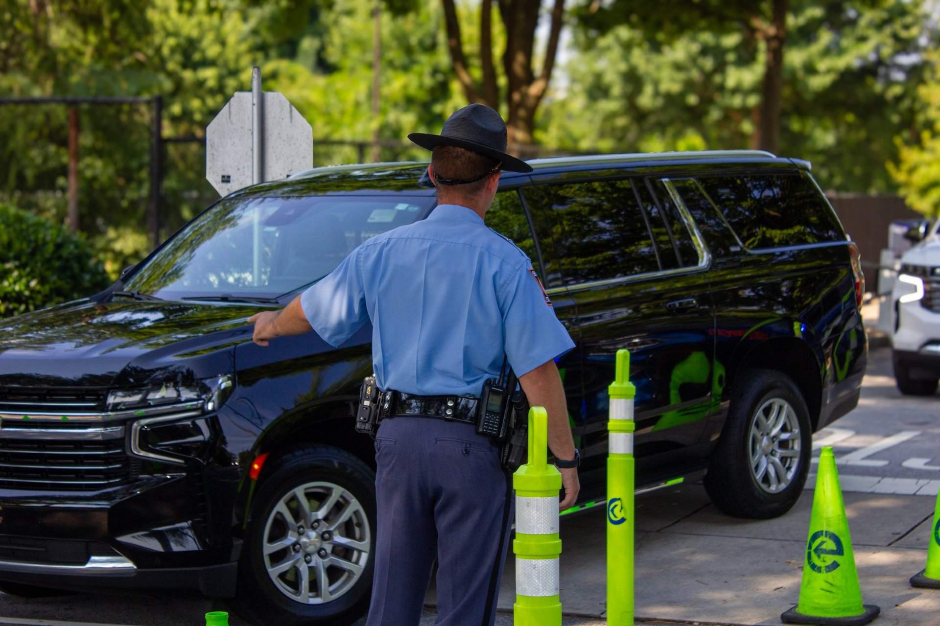 Police officer in blue uniform standing next to patrol car at traffic control checkpoint with green and white traffic cones