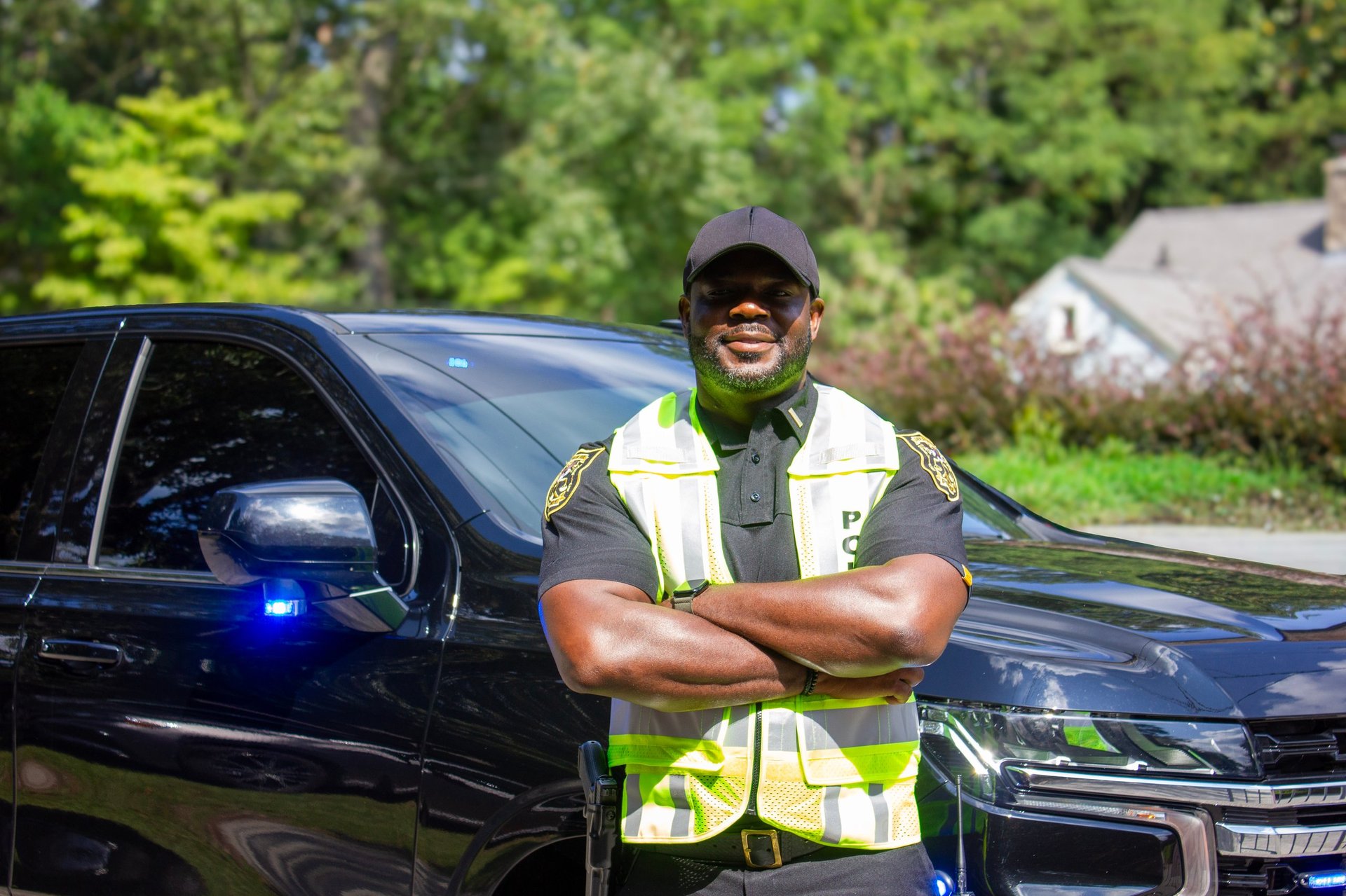Law enforcement officer in reflective safety vest standing in front of marked police vehicle with arms crossed