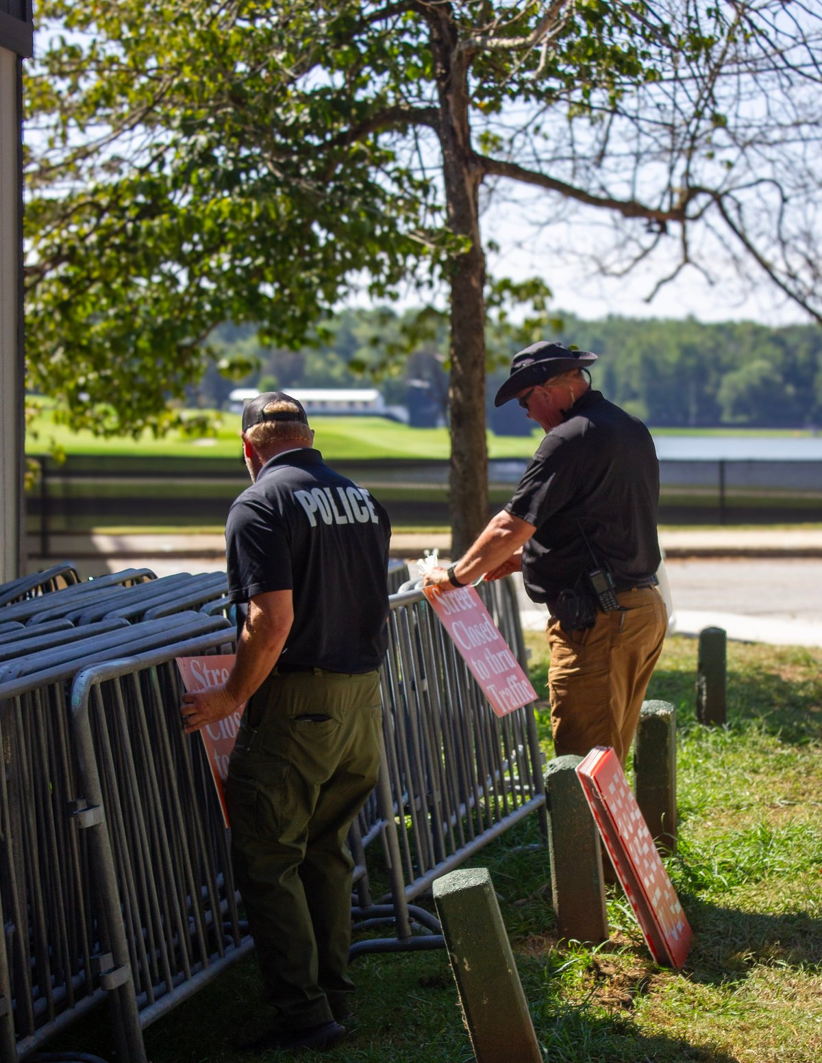 Police officer and man setting up metal crowd control barriers by a waterfront park on a sunny day