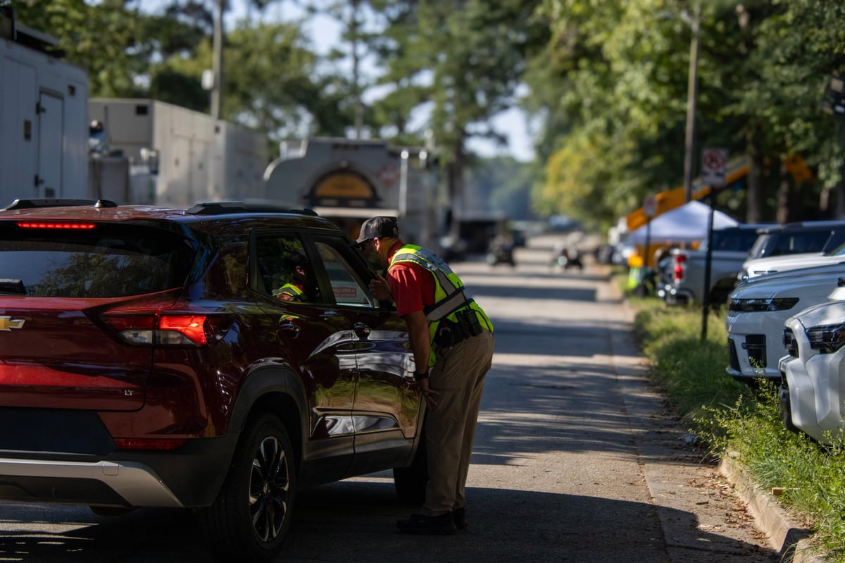 Officer in uniform conducting a traffic stop on a red SUV parked on a residential street with trees and houses in the background