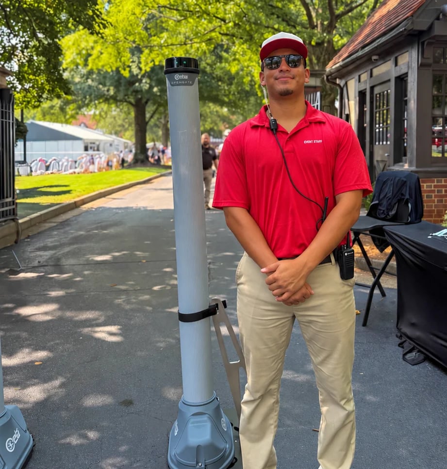 Man in red polo shirt and baseball cap standing next to a gray parking meter on a tree-lined street