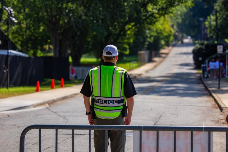 Police officer in neon green reflective vest standing behind metal barricade on residential street
