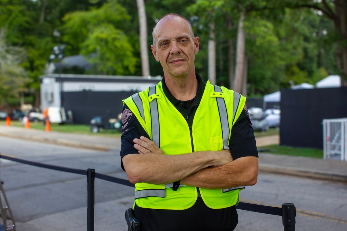 Construction or security worker in neon yellow safety vest with arms crossed, standing outdoors at a worksite