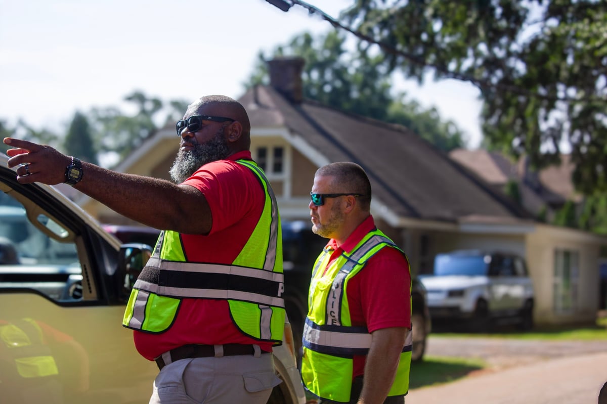 Two workers in red shirts and yellow safety vests examining a large piece of equipment or material outside a residential house